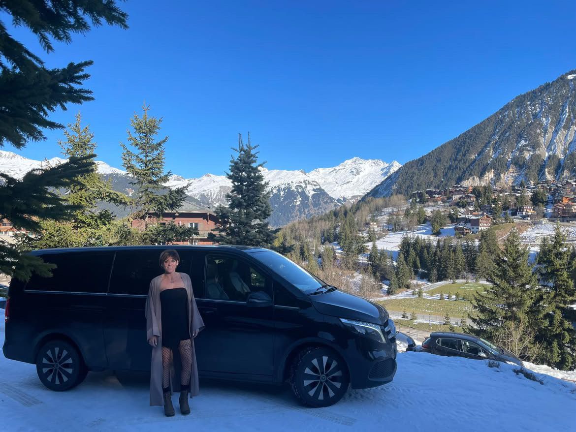 Madame Drive devant son van noir, avec vue sur Courchevel enneigé